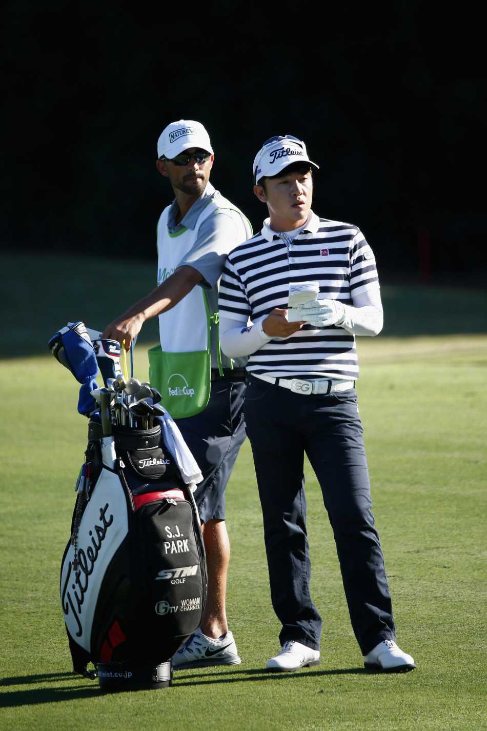 泰格·伍兹在果岭边全神贯注地审视推杆路线，阳光洒在他的背影上，仿佛为即将到来的关键一击镀上了一层金边。