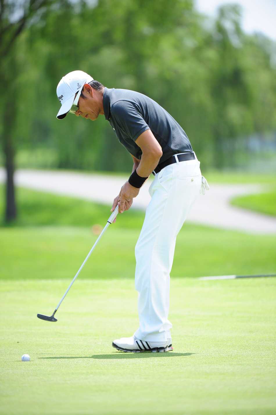 陈道明在果岭边凝神观察，阳光洒在他专注的侧脸，仿佛正在阅读大地与草纹的细微语言，谋划下一杆的精准路径