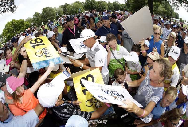 冠军球员菲尔·米克尔森正在为一位年轻球迷签名，他微微低头，神情温和，展现出巨星的亲和一面。