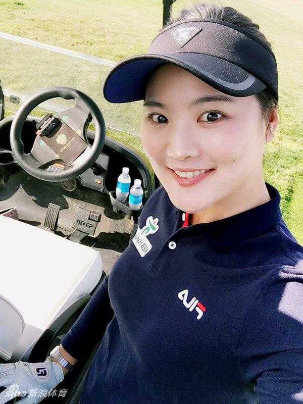 柳箫然身着淡蓝长裙立于果岭边缘，霞光为她镀上金边，宛如从高尔夫史诗中走出的女神