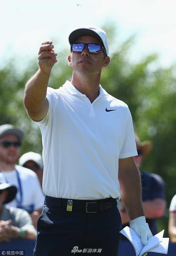 卡西在风中扬起草屑测风向，侧脸专注，背景是广阔的球场与天空