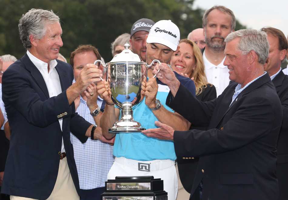 毕耶加斯与赛事官员共同展示巨型冠军支票，身后是欢呼的观众，喜悦与成就感激荡在空气中