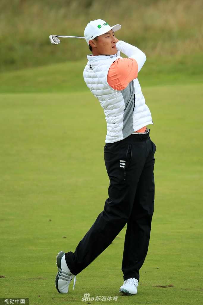 李昊桐在皇家波特拉什球场果岭边凝神观察，远处是标志性的白色赛事记分牌与观众看台，经典的海滨林克斯风貌尽收眼底。