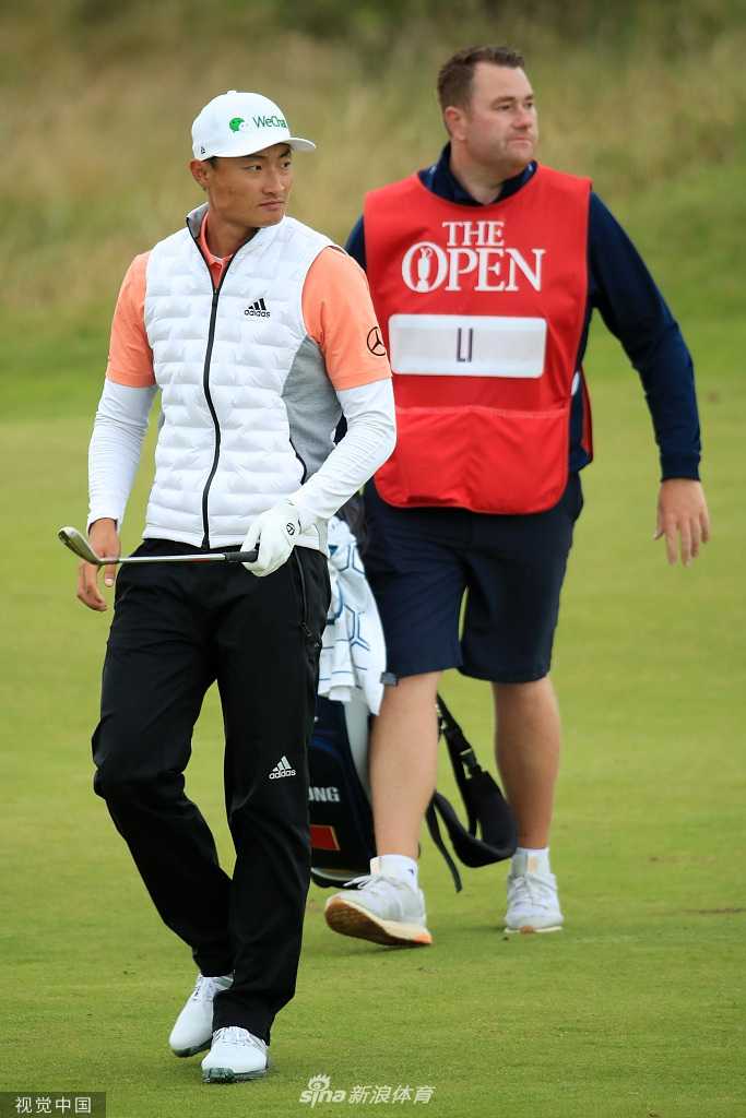 李昊桐走向开球台，身后是英国公开赛巨大的金色标志牌，现场氛围庄重而充满历史感。