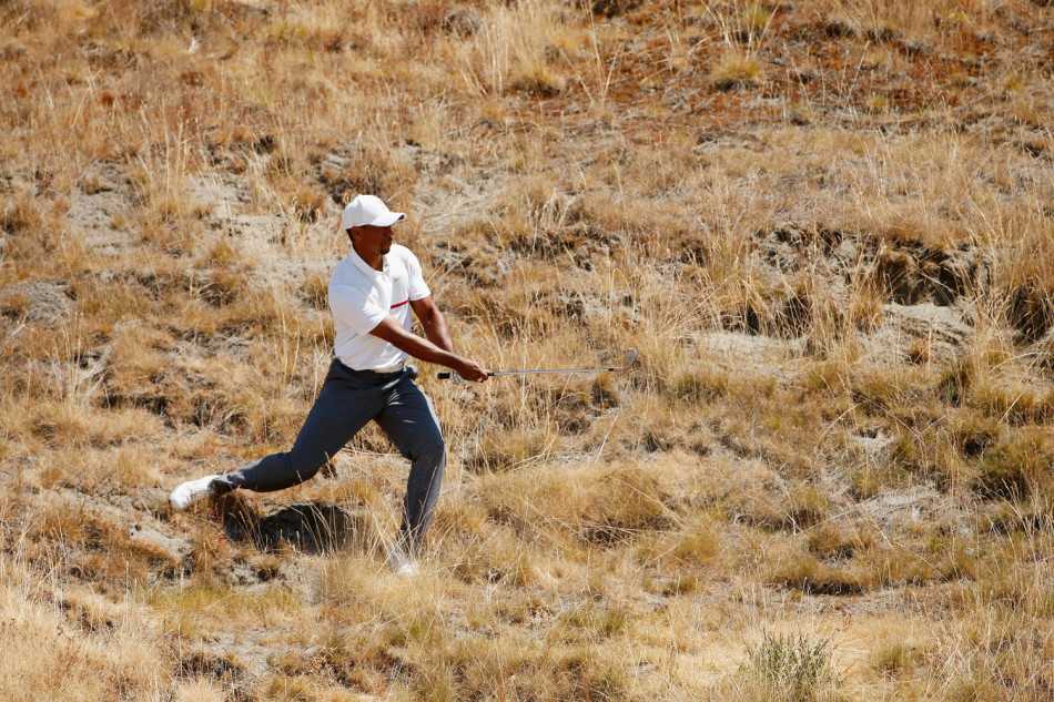老虎伍兹屈膝俯身于沙坑边缘，目光如炬地凝视着埋藏于细沙中的小球，全神贯注地计算着解救它的最佳路径。